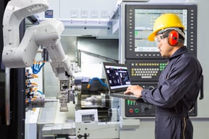 Engineer using laptop computer for maintenance automatic robotic arm with CNC machine in smart factory